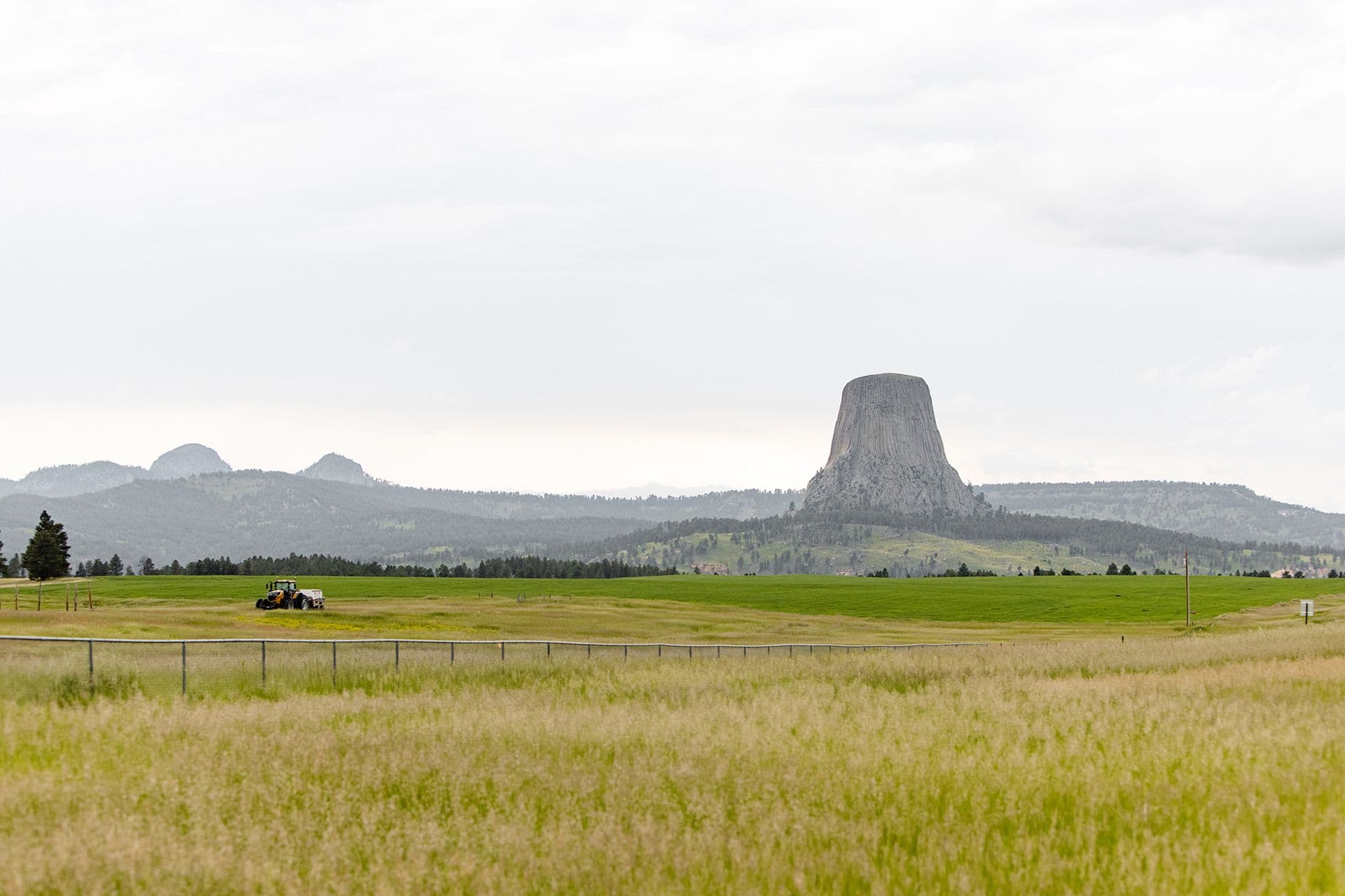 Green field with a tractor in front of mountain skyline with a big rock